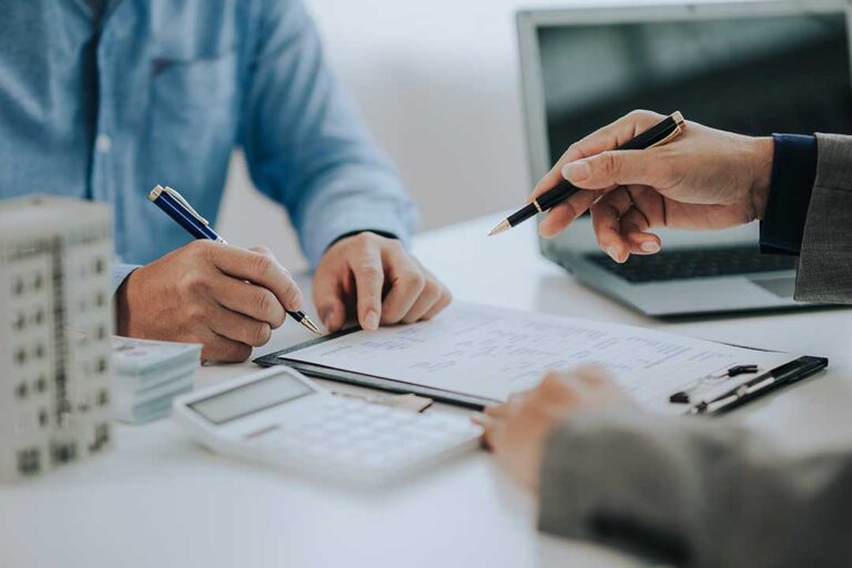 A couple reviews life insurance documents and a calculator at a kitchen table.