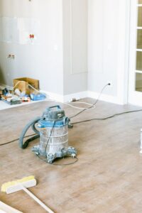 Homeowner examines water stains on a ceiling beside a bucket and damp flooring after a plumbing leak.